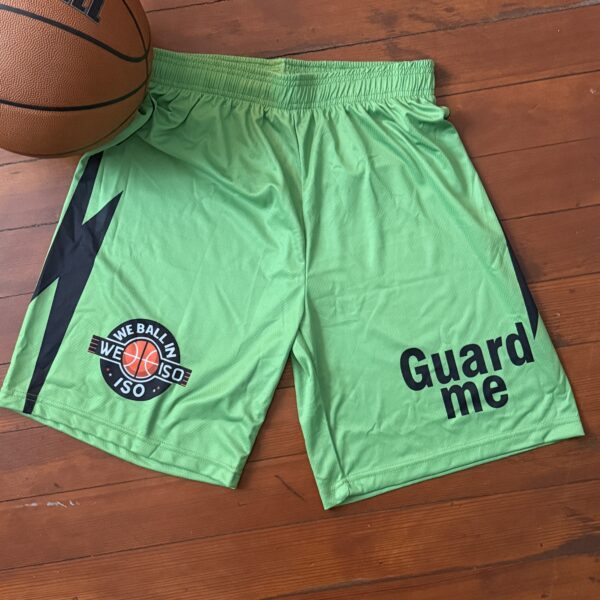 Green basketball shorts with logos and text, laid flat on a wooden floor.