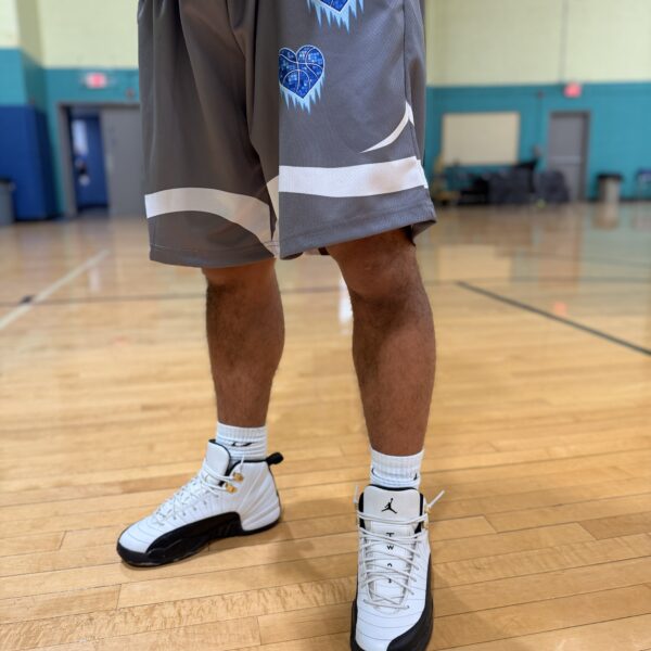 Person wearing basketball shorts and sneakers standing on a gym floor.