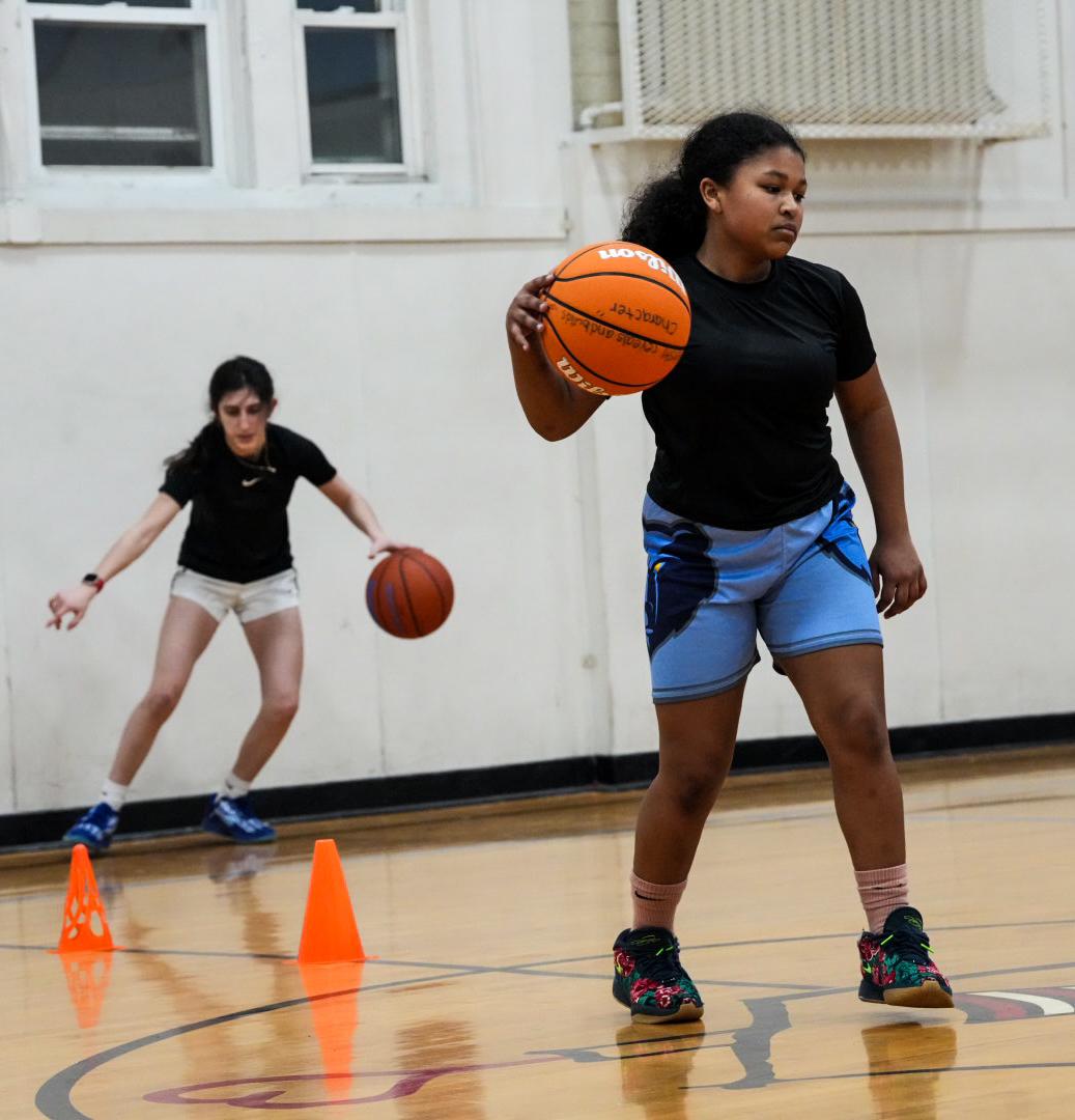 Two girls practicing basketball dribbling drills in a gym.