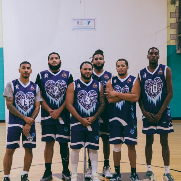 Six basketball players pose in matching black and purple uniforms on an indoor court.