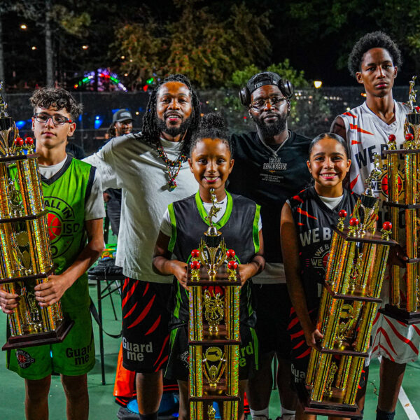 Six young people proudly holding traditional trophies outdoors at night.