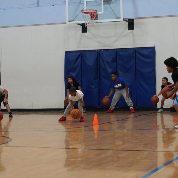Children practicing basketball drills with cones in a gymnasium.