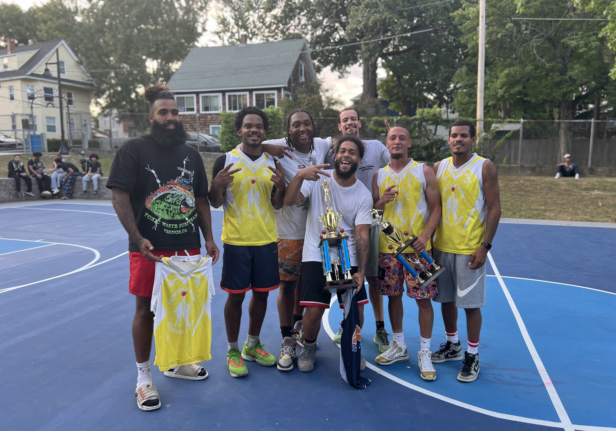 A group of seven men posing on a basketball court with trophies.