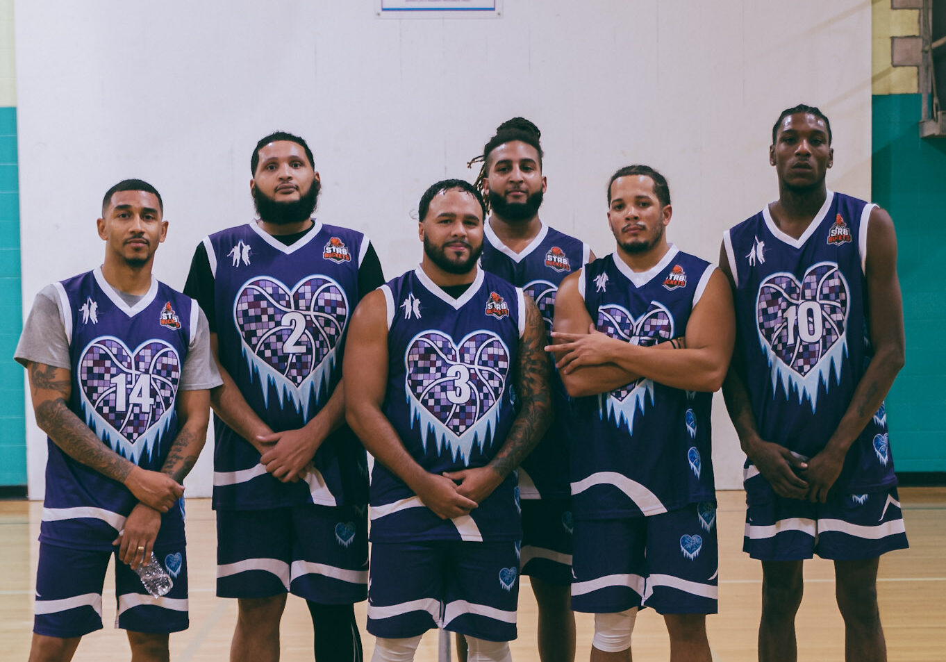 Six basketball players pose in matching black and purple uniforms on an indoor court.