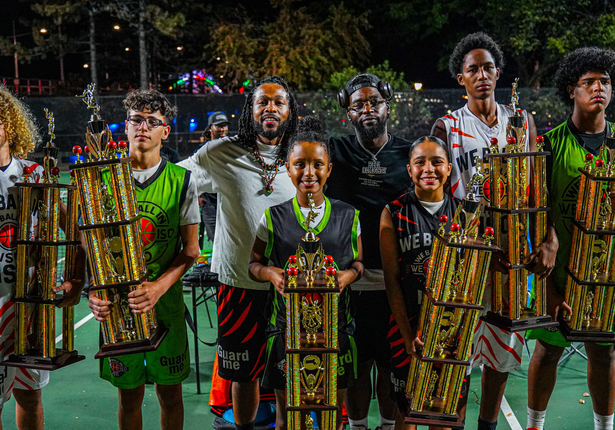 Six young people proudly holding traditional trophies outdoors at night.