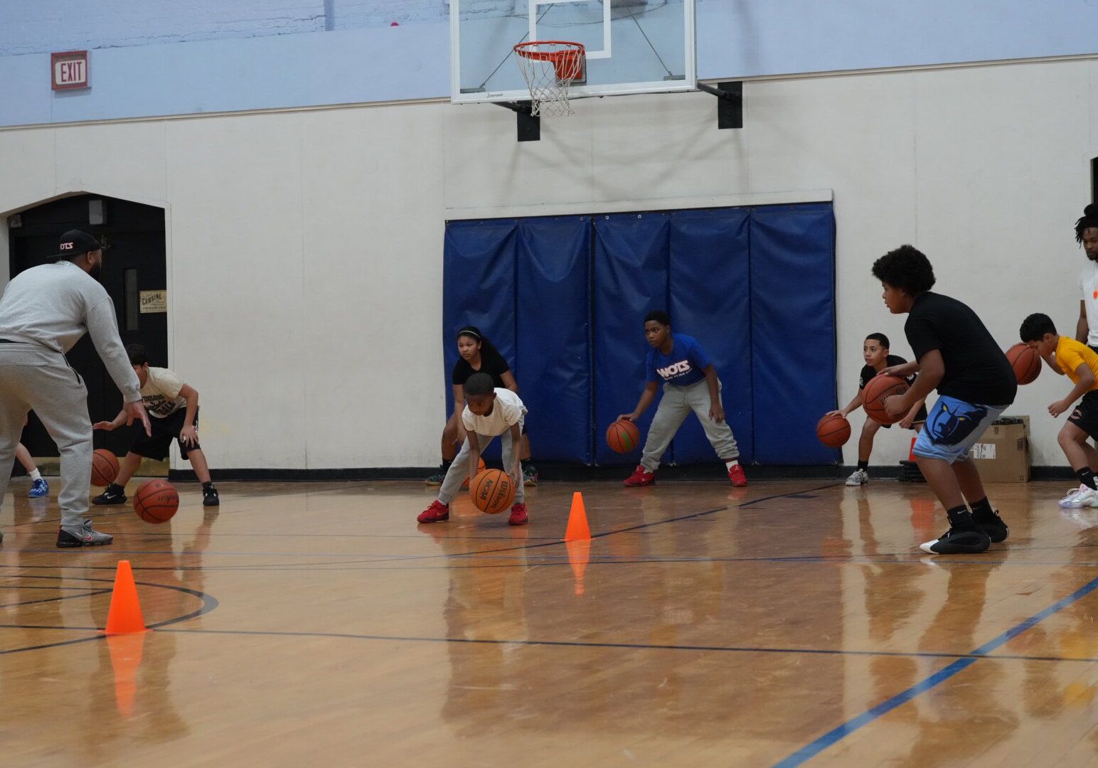 Children practicing basketball drills with cones in a gymnasium.